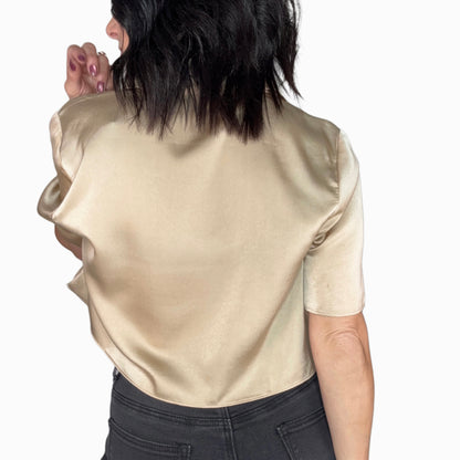 Back profile of a woman wearing a gold satin blouse and dark jeans on a white background