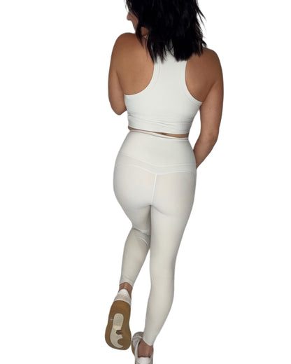 Back profile of a woman wearing a off white athletic outfit on a white background