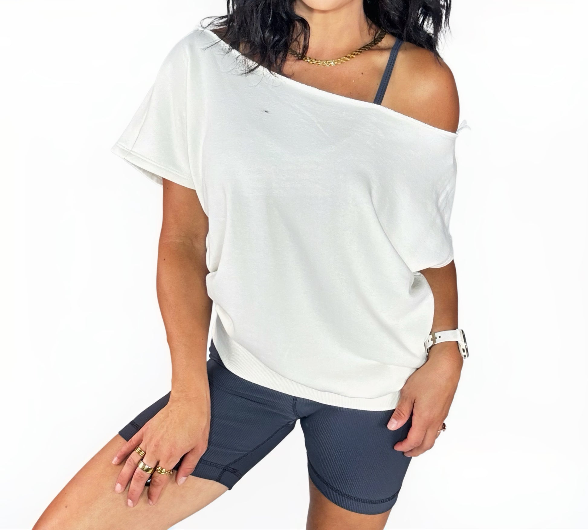 Person wearing a white off-shoulder top and dark shorts on a plain background