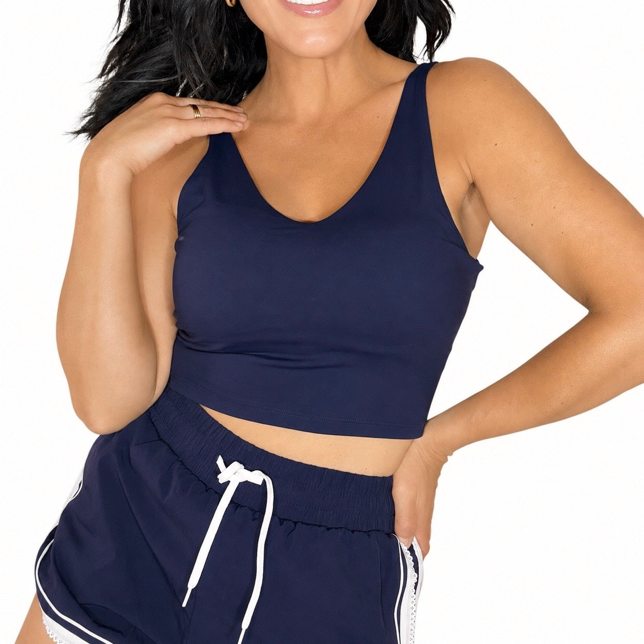 Close up of a woman wearing a navy sports tank and matching navy shorts with white trim on a white background 