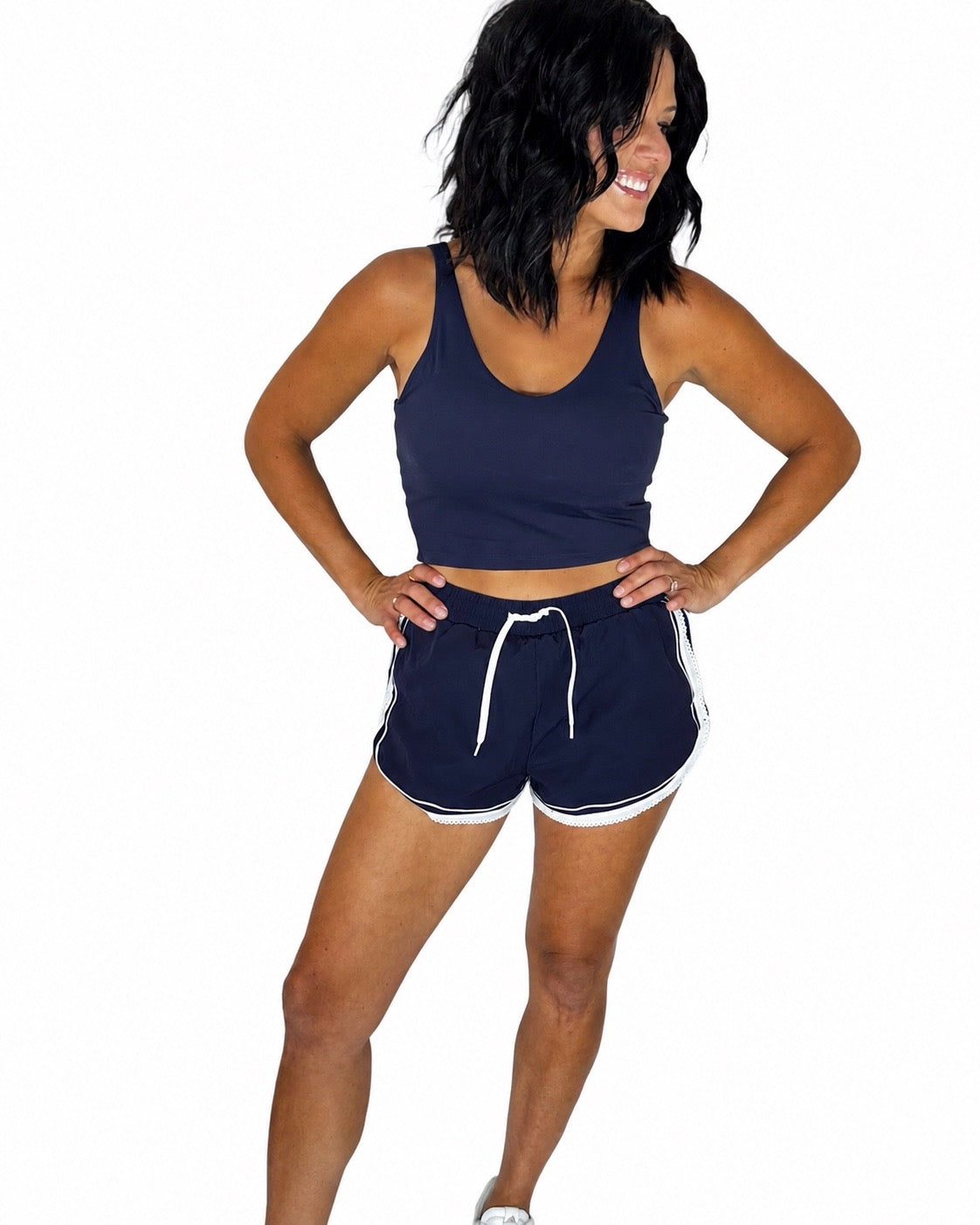Woman wearing a navy active tank paired with matching navy shorts with white trimming on a white background