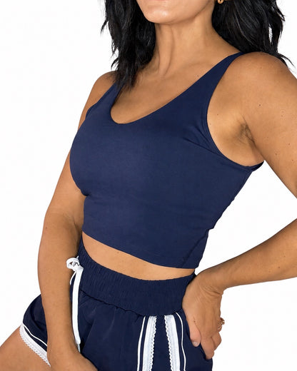 Side profile of a woman wearing a navy active tank and navy matching shorts with white lace trim on a white background