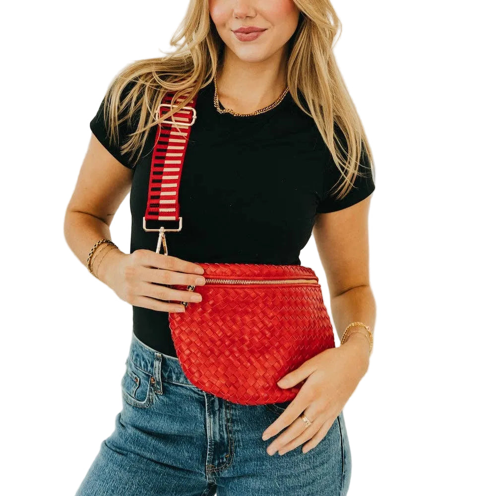 Woman wearing a red woven fanny pack with a striped strap on a plain background